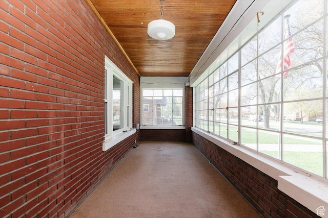 unfurnished sunroom with wooden ceiling, carpet, and brick wall