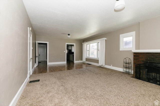 unfurnished living room with a brick fireplace, baseboards, visible vents, and carpet