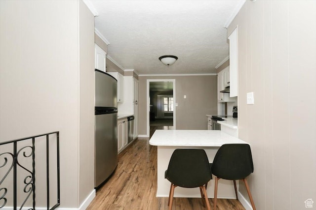 kitchen with a peninsula, light countertops, white cabinetry, light wood finished floors, and appliances with stainless steel finishes