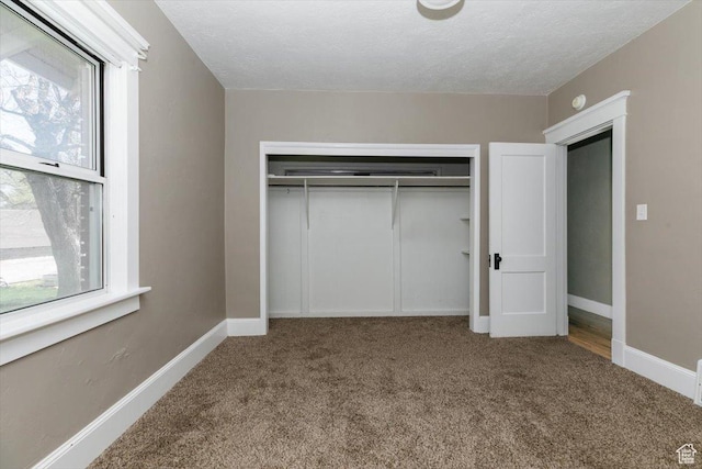 unfurnished bedroom with a closet, a textured ceiling, carpet, and baseboards