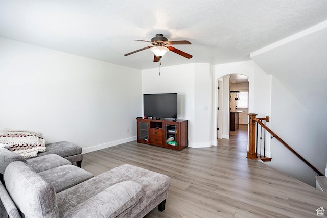 living area featuring a ceiling fan, light wood-style flooring, baseboards, and arched walkways
