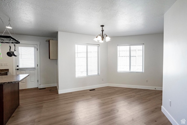 unfurnished dining area with a textured ceiling, a chandelier, visible vents, baseboards, and wood finished floors