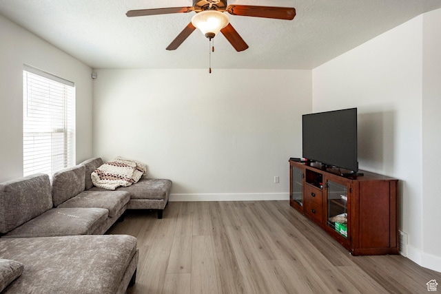 living room with a ceiling fan, baseboards, a textured ceiling, and light wood-style floors