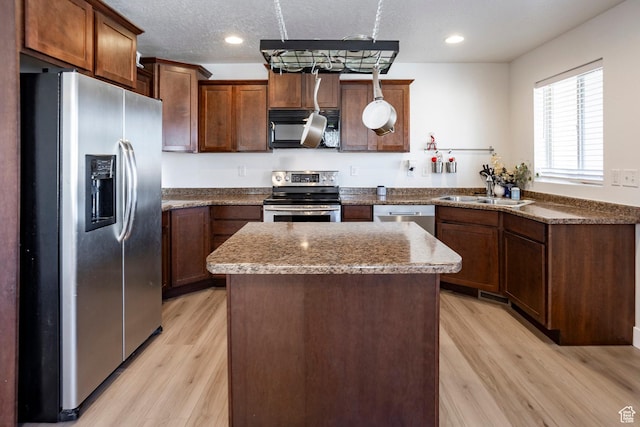 kitchen with recessed lighting, stainless steel appliances, light wood finished floors, a sink, and a center island