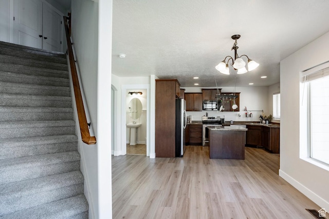 kitchen featuring appliances with stainless steel finishes, an inviting chandelier, light wood-style floors, and a center island