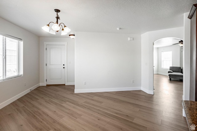 unfurnished room featuring light wood-type flooring, baseboards, a notable chandelier, and arched walkways