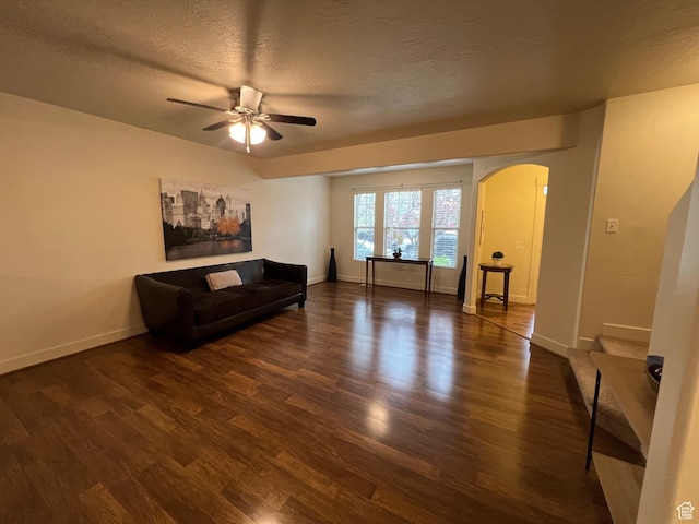 living room with arched walkways, a textured ceiling, a ceiling fan, baseboards, and wood finished floors