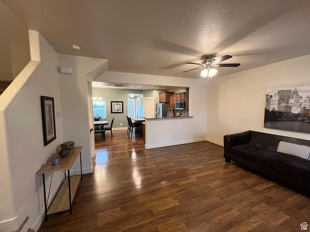 living room featuring baseboards, a textured ceiling, dark wood finished floors, and ceiling fan with notable chandelier