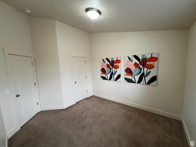 empty room with baseboards, dark colored carpet, and a textured ceiling