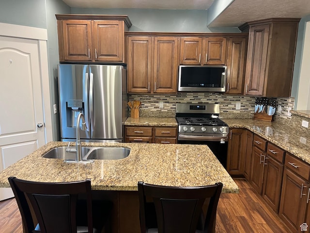 kitchen with dark wood-style flooring, an island with sink, tasteful backsplash, a sink, and stainless steel appliances