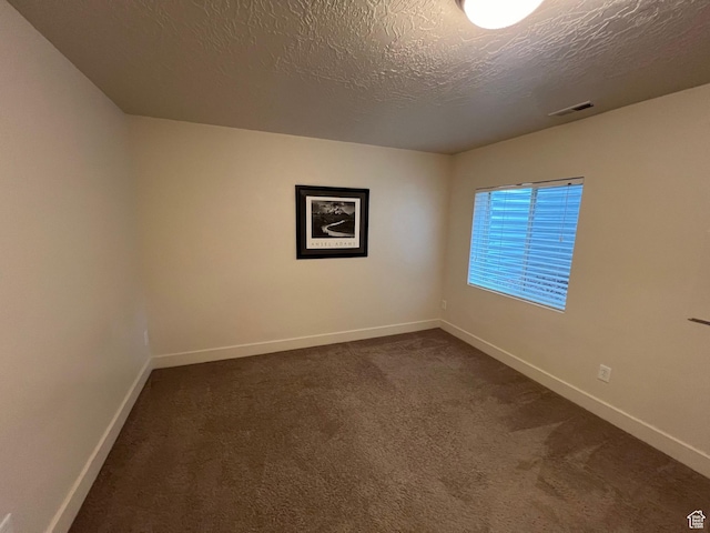 empty room featuring visible vents, a textured ceiling, baseboards, and dark carpet