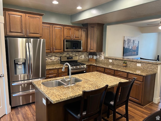 kitchen featuring a peninsula, dark wood-style floors, a sink, appliances with stainless steel finishes, and backsplash