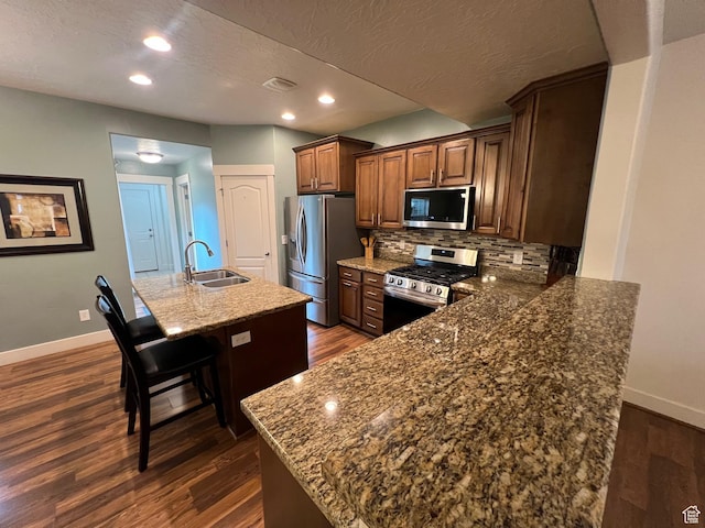 kitchen with dark wood-style flooring, appliances with stainless steel finishes, a sink, baseboards, and a kitchen bar