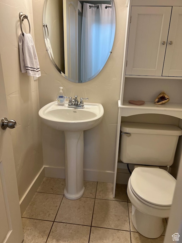 half bathroom with toilet, baseboards, a sink, and tile patterned flooring