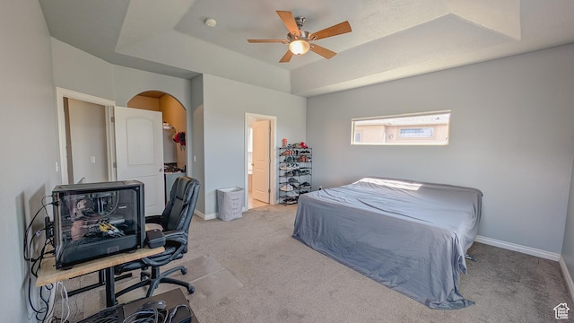 bedroom with baseboards, a raised ceiling, arched walkways, and light colored carpet