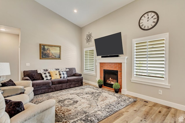living room with a brick fireplace, high vaulted ceiling, visible vents, baseboards, and wood finished floors