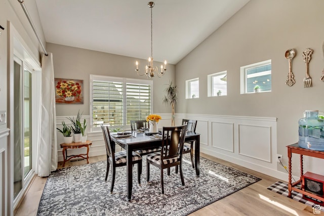 dining space featuring light wood-type flooring, a wainscoted wall, a notable chandelier, and lofted ceiling