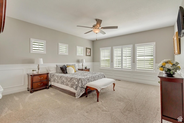 carpeted bedroom featuring ceiling fan, a wainscoted wall, and multiple windows