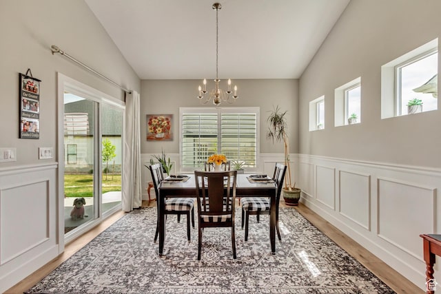dining area with a decorative wall, light wood-style floors, vaulted ceiling, a wainscoted wall, and a notable chandelier
