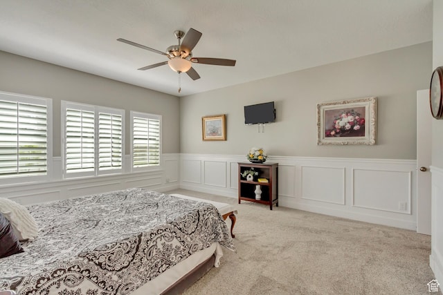 bedroom with wainscoting, ceiling fan, carpet, and a decorative wall