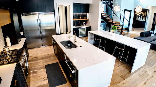 13327 S Bullitt Ln, Draper, UT 84020 - kitchen featuring light wood finished floors, a sink, dark cabinetry, high end appliances, and a large island with sink