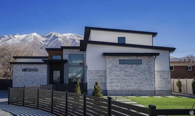 contemporary house with a mountain view, stone siding, fence private yard, and stucco siding