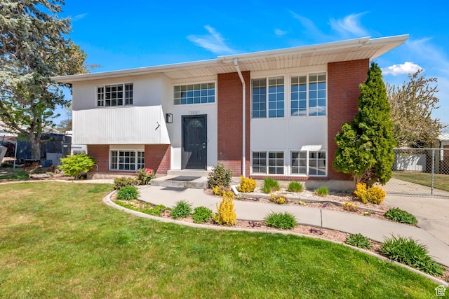 bi-level home featuring a front yard, fence, and brick siding