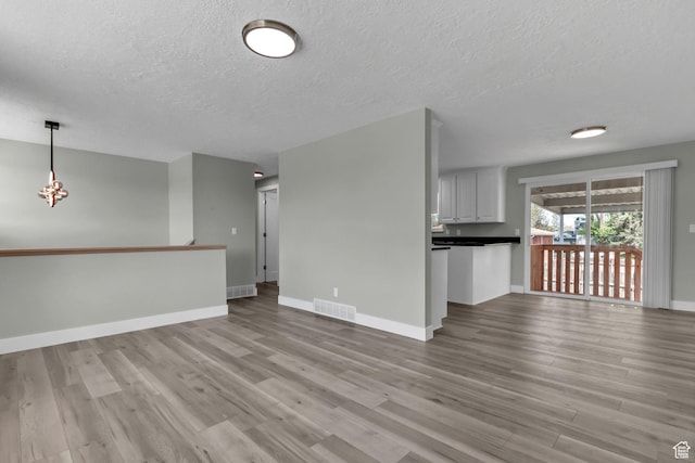 3502 W 8350 S, West Jordan, UT 84088 - unfurnished living room with light wood-type flooring, baseboards, visible vents, a notable chandelier, and a textured ceiling