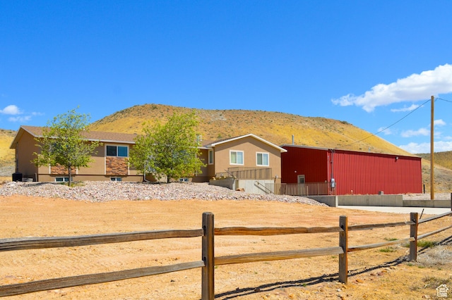 view of front of property featuring an outdoor structure, a pole building, a mountain view, stucco siding, and fence