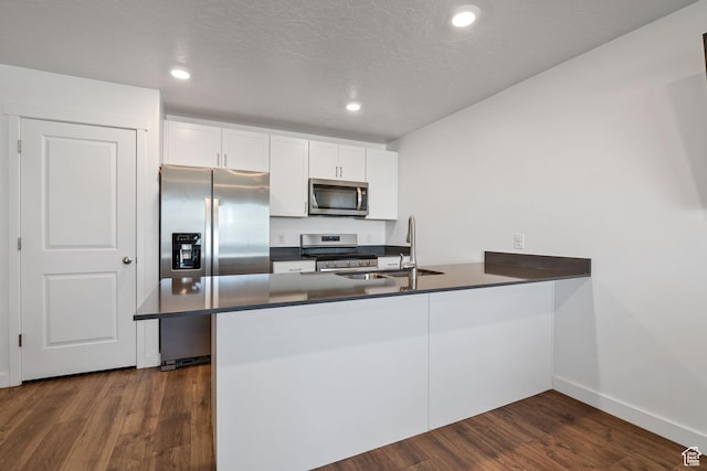 kitchen with dark wood-style floors, a sink, a peninsula, dark countertops, and appliances with stainless steel finishes