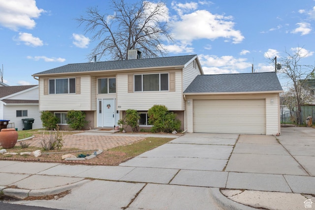 bi-level home with concrete driveway, a garage, and roof with shingles