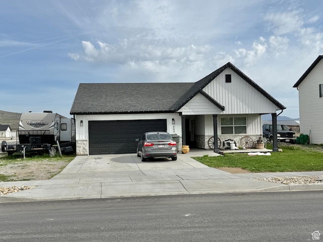 884 W Factory St, Garland, UT 84312 - view of front of house with driveway, a front lawn, an attached garage, and stone siding