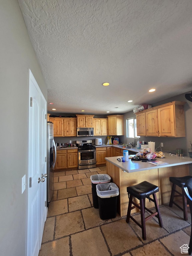 5564 S Yellow Fin Way W, Murray, UT 84107 - kitchen with a textured ceiling, stone tile flooring, stainless steel appliances, recessed lighting, and a peninsula