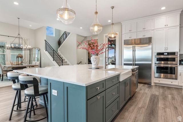4772 W Thorntree Ln, Herriman, UT 84096 - kitchen featuring a kitchen island with sink, appliances with stainless steel finishes, a sink, white cabinetry, and light wood-type flooring