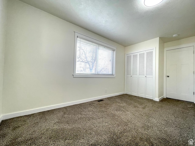 unfurnished bedroom with a closet, dark colored carpet, and baseboards