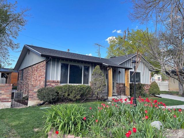 view of front of home featuring brick siding, board and batten siding, a shingled roof, and a front yard