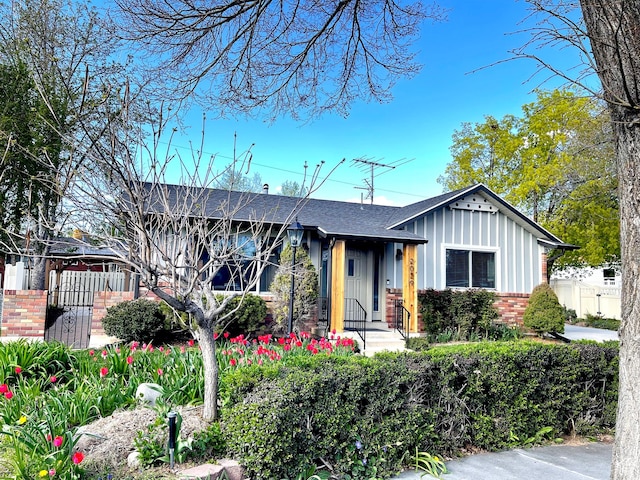 view of front facade with brick siding, board and batten siding, fence, and a shingled roof