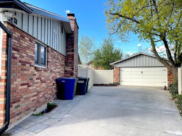 view of property exterior with brick siding, board and batten siding, a chimney, concrete driveway, and fence
