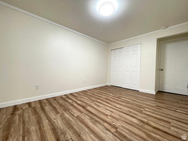 unfurnished bedroom featuring crown molding, a closet, wood finished floors, and baseboards