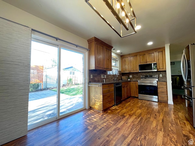 kitchen with dark countertops, stainless steel appliances, dark wood-style flooring, brown cabinetry, and backsplash