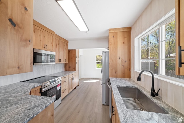 kitchen featuring light stone countertops, light brown cabinets, light wood-style flooring, appliances with stainless steel finishes, and a sink