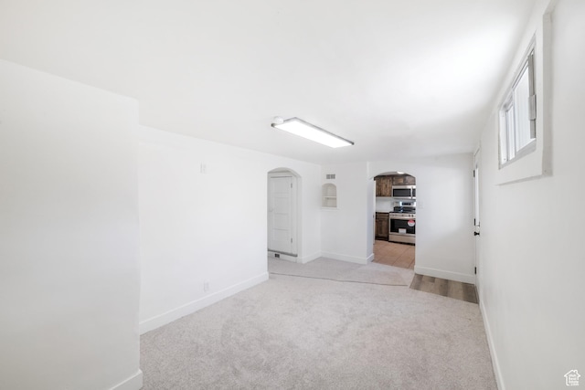 unfurnished room featuring baseboards, arched walkways, and light colored carpet
