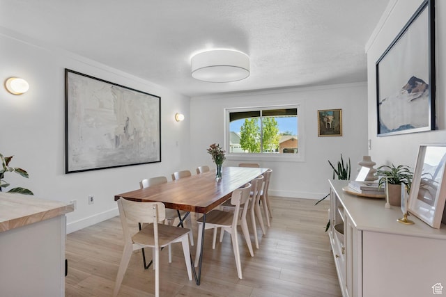 dining area featuring ornamental molding, light wood finished floors, a textured ceiling, and baseboards