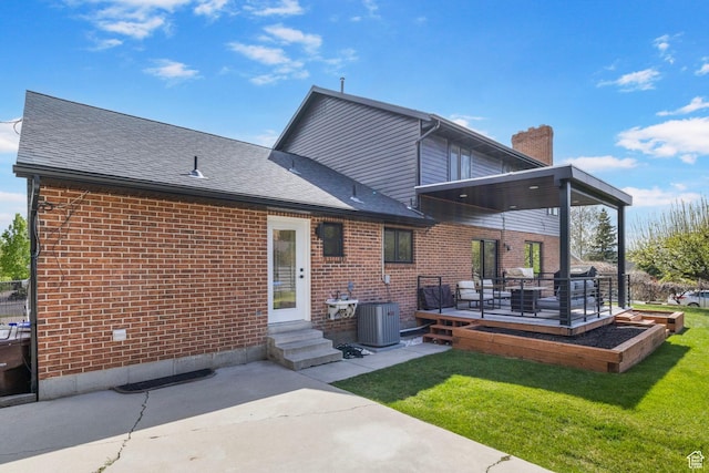 back of house featuring a chimney, a yard, brick siding, a shingled roof, and central AC unit