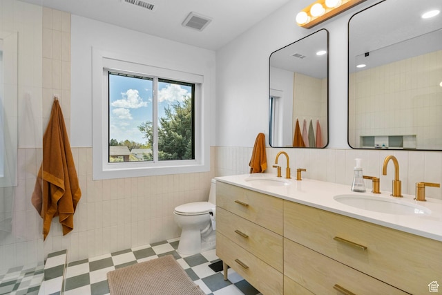 bathroom featuring toilet, tile walls, a sink, and double vanity