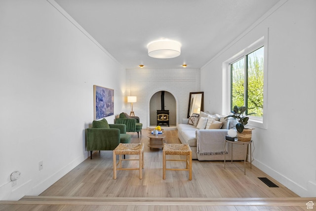 sitting room featuring visible vents, wood finished floors, a wood stove, and crown molding