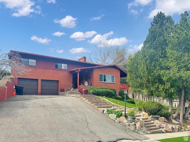 view of front of house featuring a chimney, brick siding, fence, driveway, and an attached garage