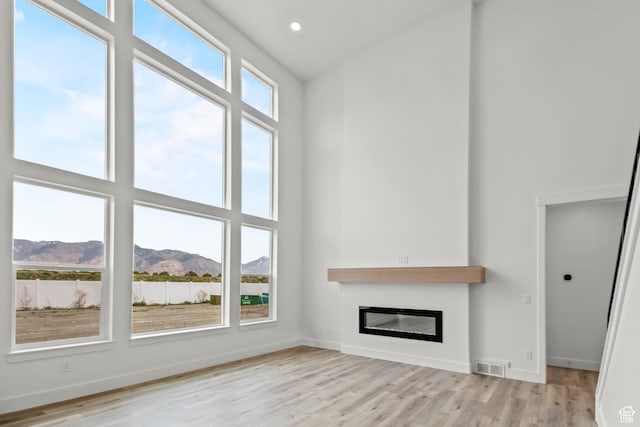 2372 W 2950 N Unit 108, Farr West, UT 84404 - unfurnished living room featuring visible vents, a high ceiling, light wood-style flooring, and a glass covered fireplace
