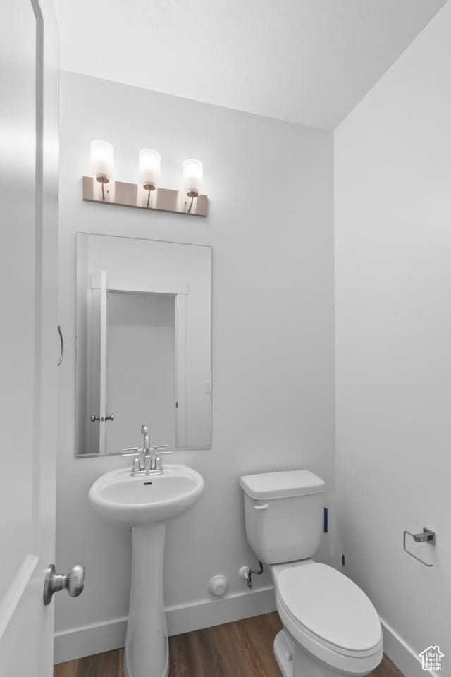 half bathroom featuring baseboards, wood finished floors, toilet, and a sink