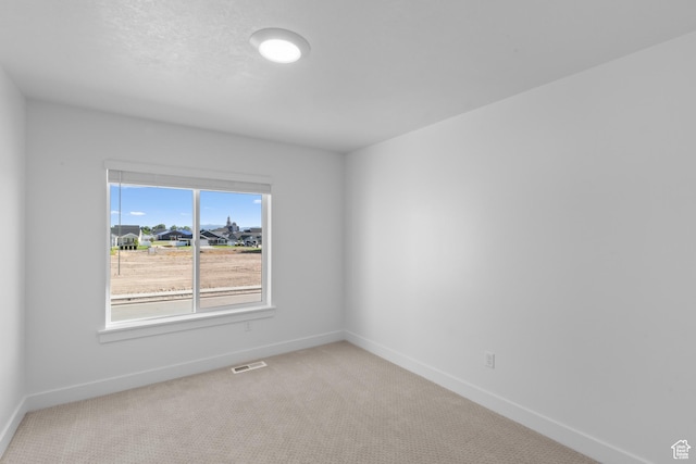 spare room with carpet floors, visible vents, and baseboards